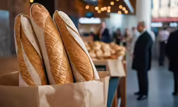 fresh bread in a paper bag placed on wooden table with people in background