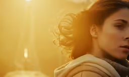a woman stands outside during the sun with her hair blowing in the wind