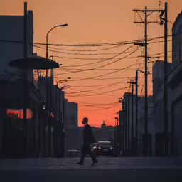 the person is walking down the sidewalk as the sun sets