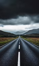 a long straight road with white lines and mountain background