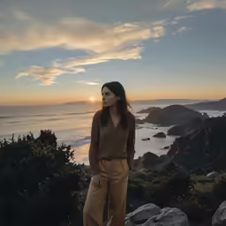 a woman in brown looking out over a rocky coast