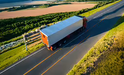 an orange and white semi truck traveling down the road,a tractor trailer truck driving along the country side