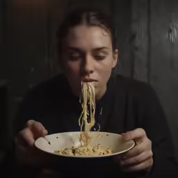 a woman in black shirt eating noodles from a bowl
