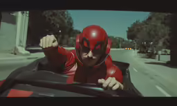 a man in a costume and a red mask driving a vehicle