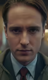 a man in a jacket and tie looking at the camera