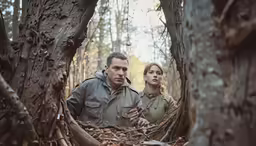 a man and a woman standing among branches and trees