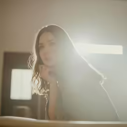woman leaning on a bed staring intently into the camera
