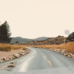 the road is empty of people as it sits near some rocks and dry grass
