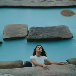 a woman sitting on a rock formation in a hot spring