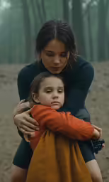 a woman hugging a little girl who is wrapped in a blanket