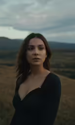 a woman in a black shirt is standing on a grassy hill