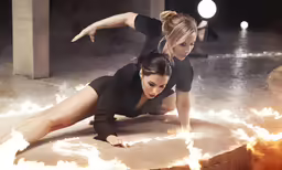 two women are dancing with fire in the background