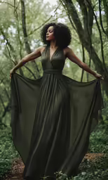 a woman wearing a green gown stands in a forest