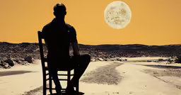 the man is sitting on a chair facing a desert road