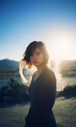 a woman standing in front of a field with the sun in the background