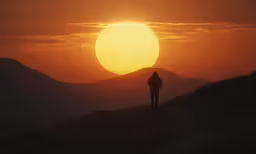a person stands on a hill with the sun in the distance