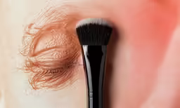 a closeup photo of an eye and a makeup brush