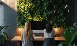 two women sitting at desk facing wall of greenery