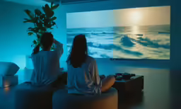 two people sitting on couches watching a movie on large screen