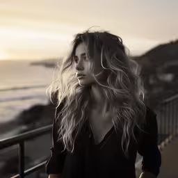 the girl is walking up to a beach,a woman with long hair stands on the balcony looking out at the ocean