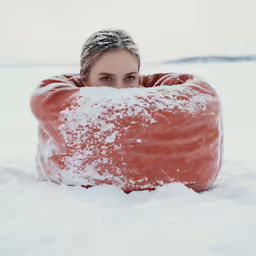 there is a woman laying in the snow, her head buried behind a large snowball