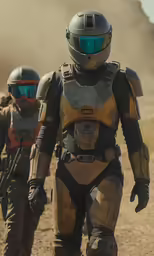 two people in helmets and protective gear walk through the desert