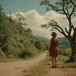 a woman is standing on the side of a dirt road