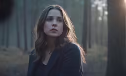 a woman looks to the side in a forest