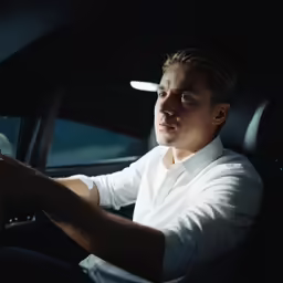 a man wearing a white shirt sits in a vehicle