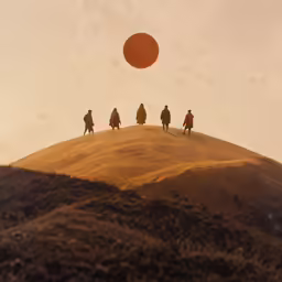 three men walking on the top of a hill towards a red ball