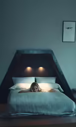 a woman is laying in bed with some lights on the headboard