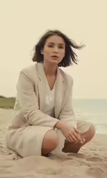 a woman is sitting in the sand and posing for a photo