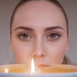 a woman stares through the lens as she holds a lit candle in her mouth