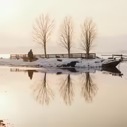 a wooden fence across a frozen lake with a boat in the distance