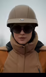 woman in tan jacket and brown helmet wearing sunglasses