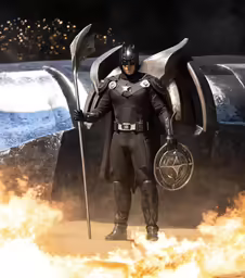 a man dressed in a batman costume holding a stick with a big flame coming out