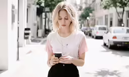 a woman standing on a city street and looking at her cell phone