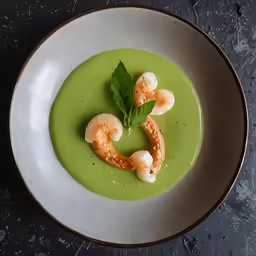 a white bowl with a green soup and shrimp garnished with parsley
