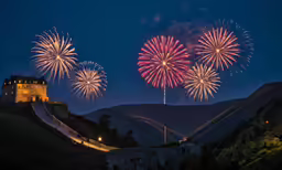 fireworks set over a castle on a hill with hills and trees behind it