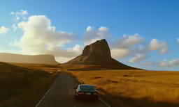 a car is driving down the road by the mountain