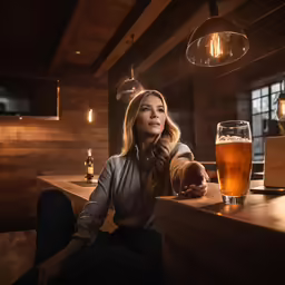 a pretty blonde woman sitting at a bar with a beer