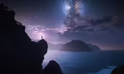 man standing on cliff looking up at stars in the sky