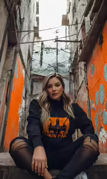 a girl wearing a black lion sweater, sheer pants, and black stockings sitting on an alley way
