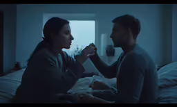 two people sitting on a bed holding hands in the dark