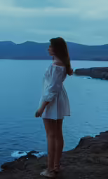 a young girl in a dress on the shore of the lake at dusk