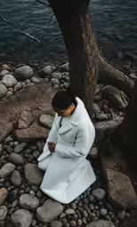the girl is dressed in white, sitting by a tree