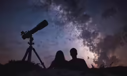 a man and woman looking at the sky with a telescope