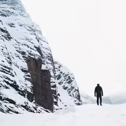 a lone person walks in the snow along the mountain side