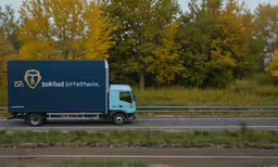 a truck is traveling down a highway near trees,the truck is traveling down the road in the sun