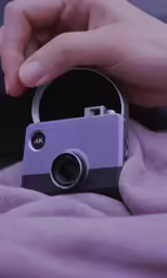 someone holding a small purple camera in the palm of their hand